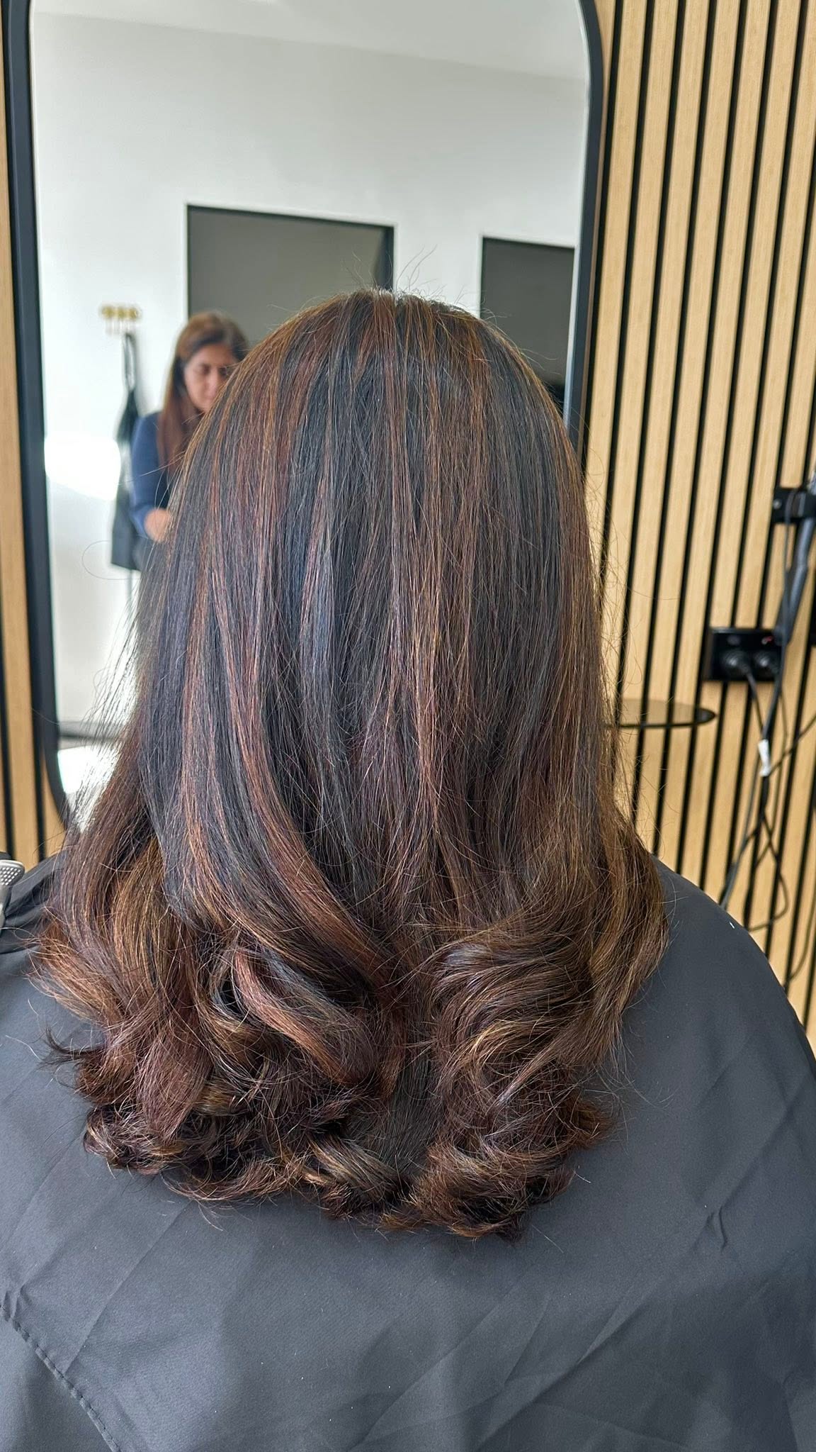 Shoulder-length dark hair with caramel highlights and soft curled ends